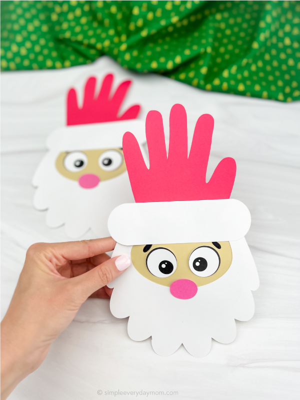 two Santa handprint cards, one in front being held to display