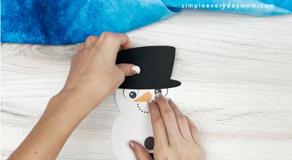 hands gluing hat to snowman card craft