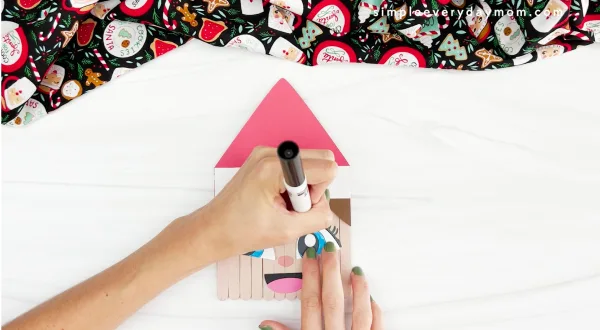 hands using a marker to draw eyelashes onto face of elf on the shelf popsicle stick craft
