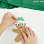 hands gluing hat onto gingerbread man card craft