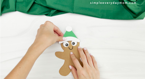 hands gluing hat onto gingerbread man card craft
