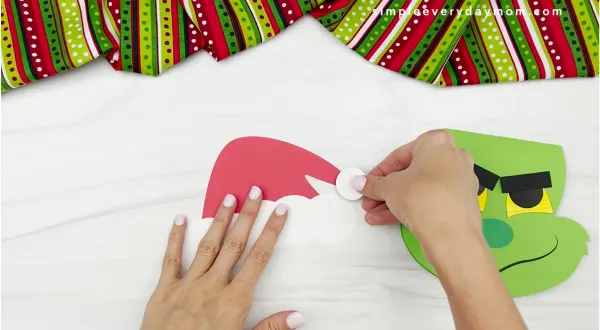 hands gluing hat pom to hat of Grinch card craft