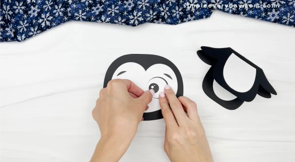 hands gluing eye to penguin card craft