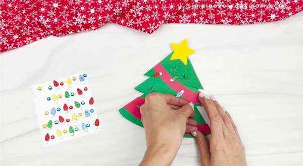 hands placing ornament stickers onto Christmas tree card craft