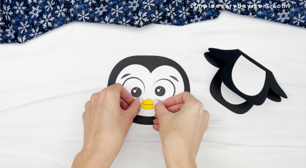 hands gluing beak to penguin card craft