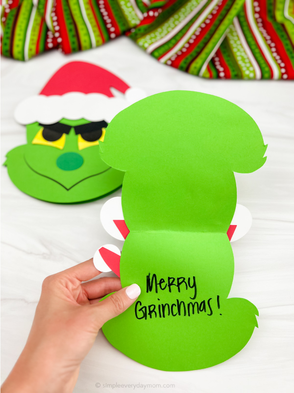 hand opening Grinch card craft with a 2nd craft in the background