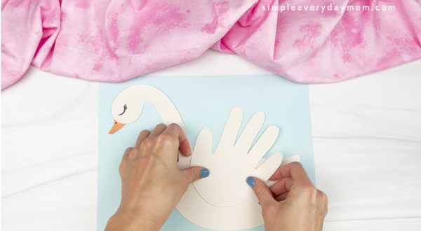 hands gluing paper handprint to swan craft