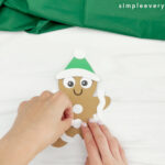 hands gluing icing buttons onto gingerbread man card craft