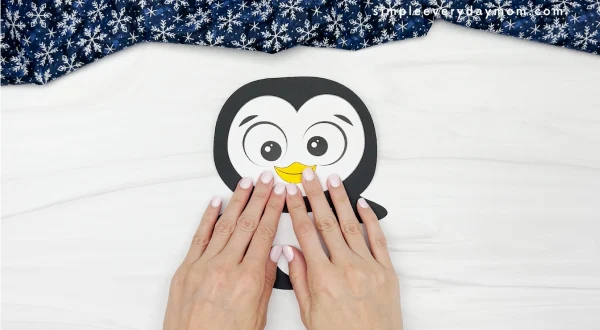 hands gluing head to body of penguin card craft