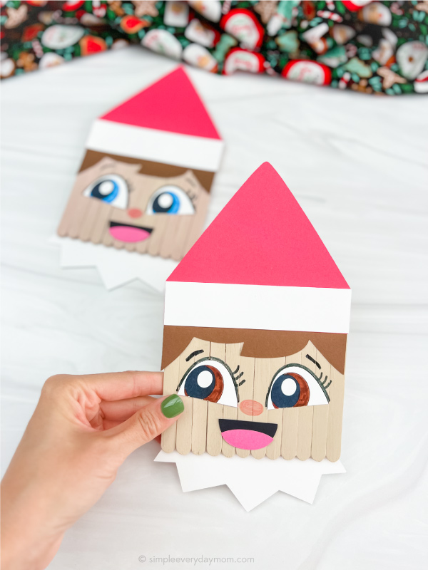hand holding finished elf on the shelf popsicle stick craft with one in foreground