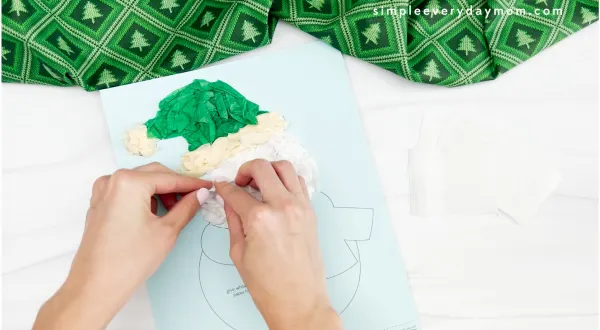 hands gluing white tissue paper to snowman craft