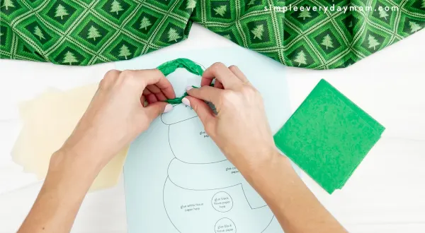 hands gluing green tissue paper to snowman craft