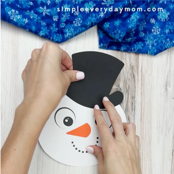 hands gluing hat to handprint snowman craft