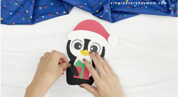 hands gluing arms to penguin Christmas craft