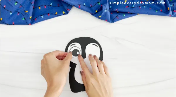 hands placing eyes onto face of Christmas penguin craft