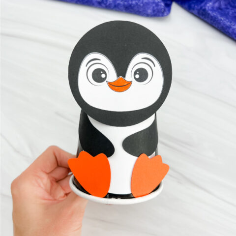 hand holding finished example of penguin paper cup craft