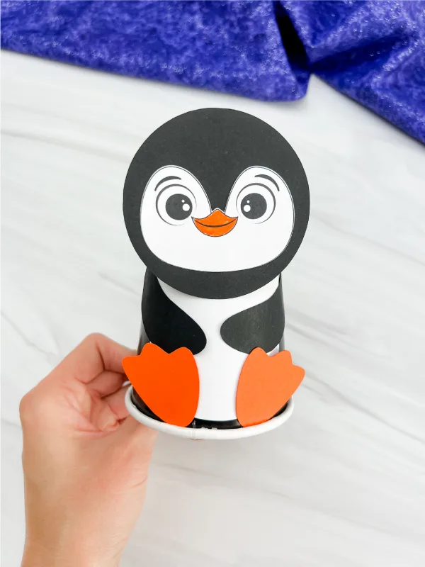 hand holding finished example of penguin paper cup craft