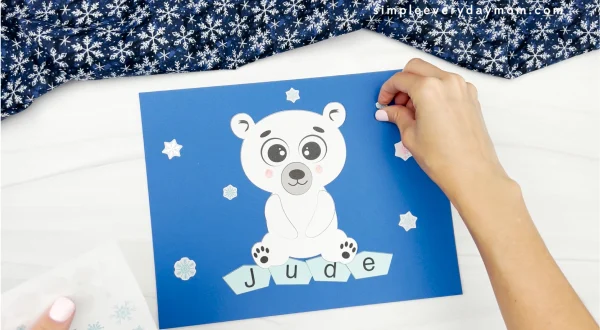 hands placing snowflake stickers onto background of polar bear name craft
