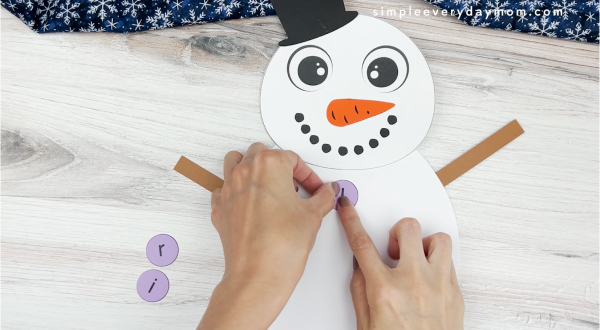 hands placing letters of name onto body of snowman name craft