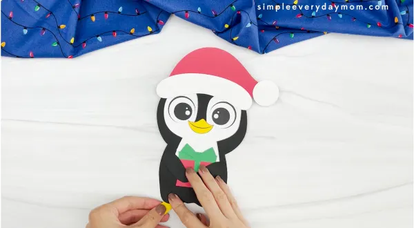 hands placing feet onto body of Christmas penguin craft