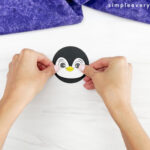 hands placing eyes onto face of penguin paper cup craft