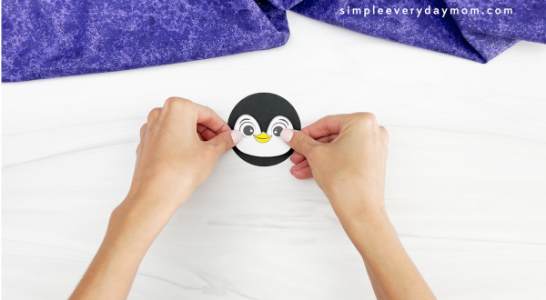 hands placing eyes onto face of penguin paper cup craft