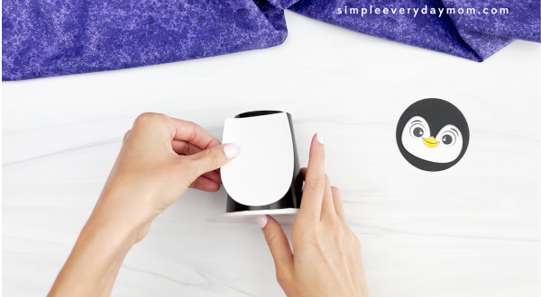 hands placing body onto cup of penguin paper cup craft