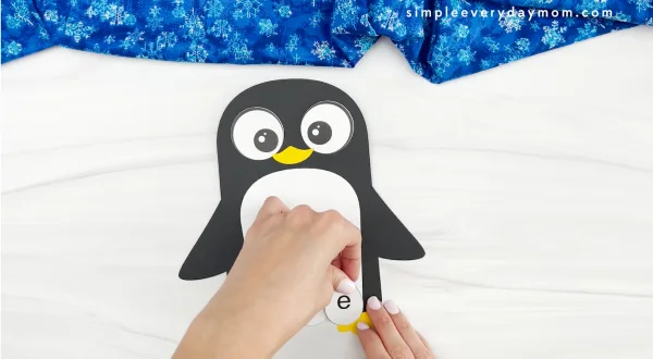 hands gluing letter eggs to bottom of penguin craft