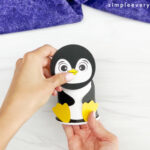 hands assembling head onto body of penguin paper cup craft