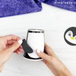 hands placing arms onto cup and body of penguin paper cup craft
