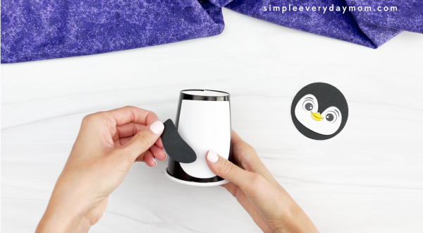 hands placing arms onto cup and body of penguin paper cup craft