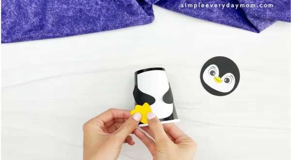 hands placing penguin feet onto cup of penguin paper cup craft