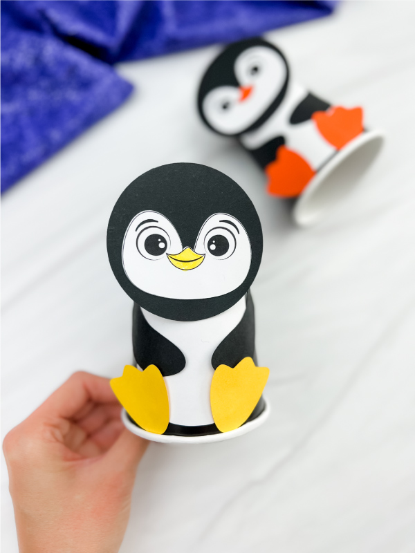 hand holding a finished example of penguin paper cup craft