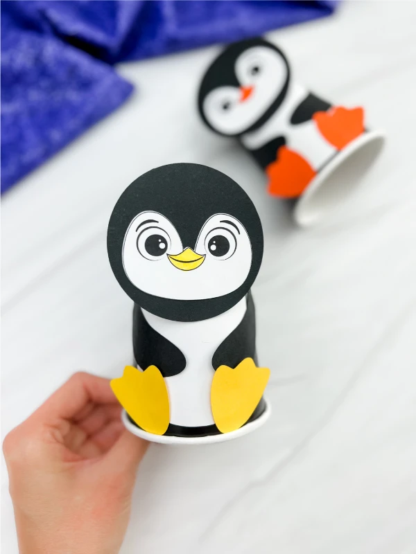 hand holding a finished example of penguin paper cup craft