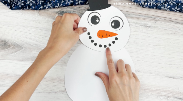 hands assembling head onto body of snowman