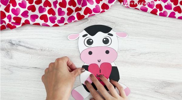 hands assembling part of arm onto body of cow valentine craft