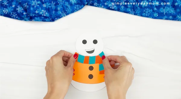 hands placing finished scarf onto body of Sneezy the snowman