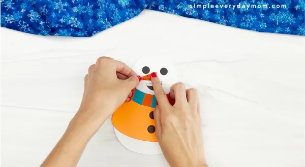 hands placing carrot onto face of Sneezy the snowman