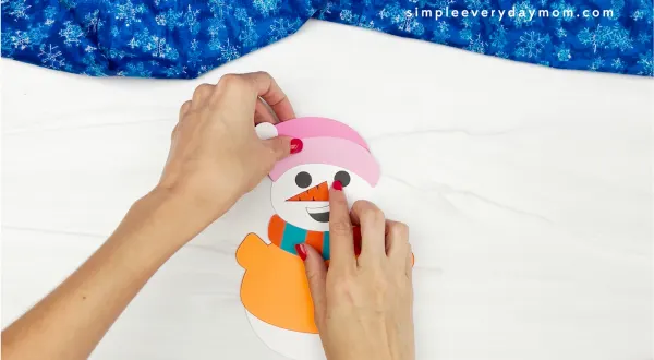 hands placing hat onto Sneezy the snowman