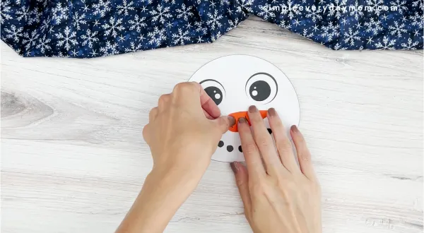 hands gluing carrot nose onto face of snowman