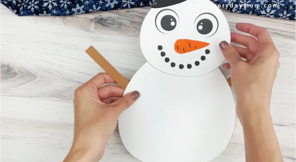 hands placing arms of snowman onto body