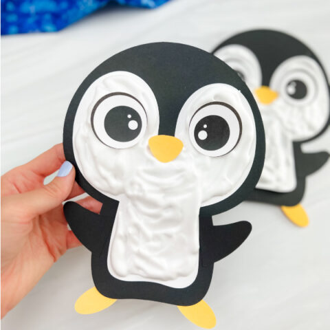 hand holding the puffy paint penguin craft with background of craft