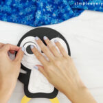 hand gluing the eyes of the puffy penguin craft