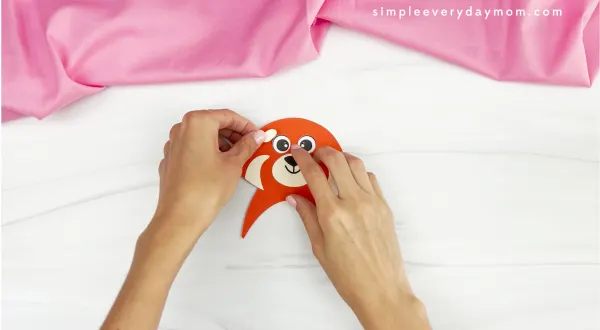 hands placing pieces of red panda onto face