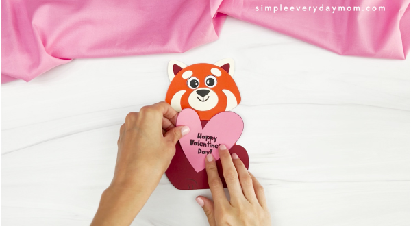 hands gluing valentine heart onto body of red panda