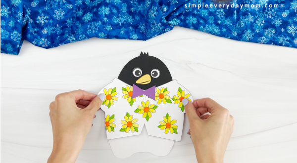 hands assembling shirt onto body of Tacky the penguin
