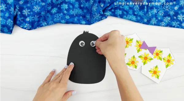 hands placing googly eyes onto face of Tacky the penguin