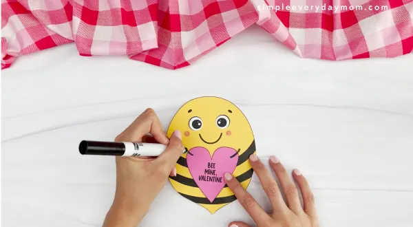 hands using a black marker to draw onto bee