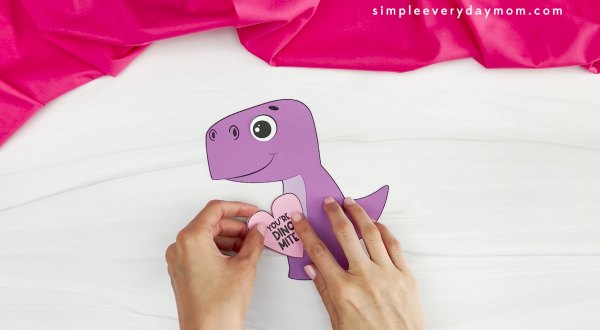 hands placing heart with valentine message onto dinosaur