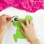hand gluing an eye onto frog face